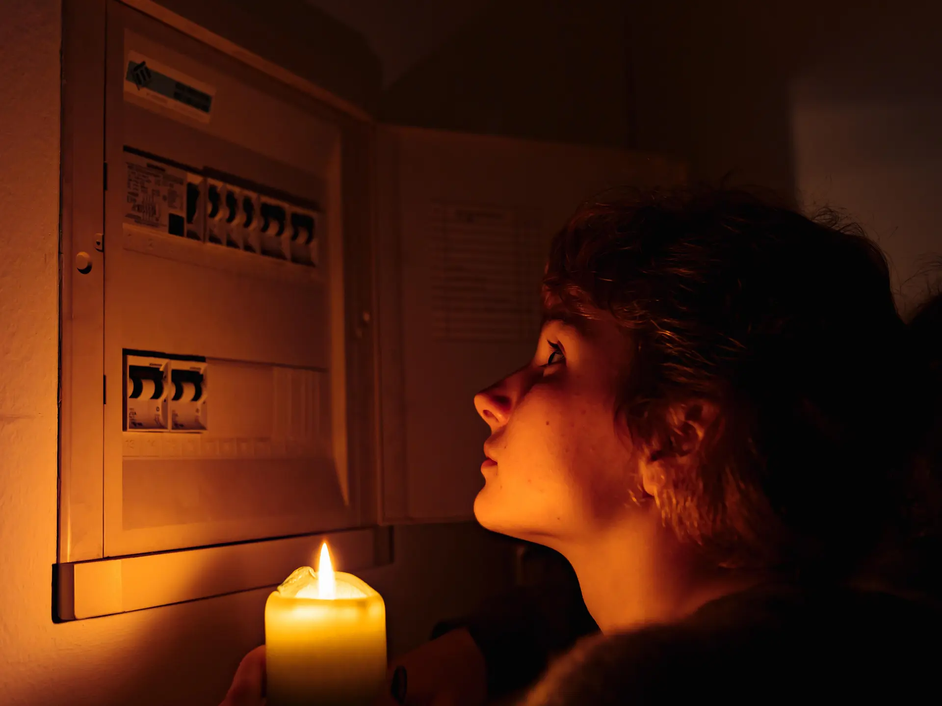 Eine Frau im Dunkeln mit einer Kerze in der Hand vor einem Stromkasten.