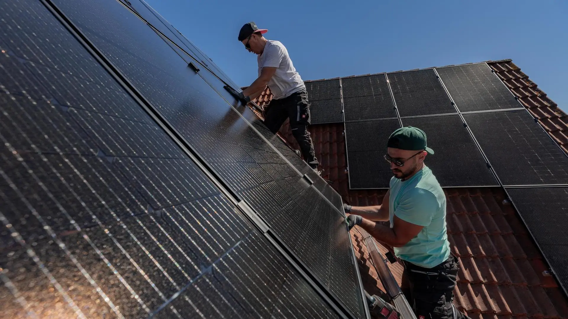 Zwei Solarwatt-Installateuren installieren auf einem Hausdach Solarmodule.