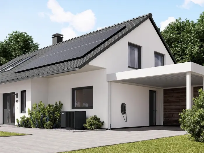 Solaranlage auf einem Hausdach eines Einfamilienhauses zusammen mit davor stehender Wärmepumpe und Wallbox