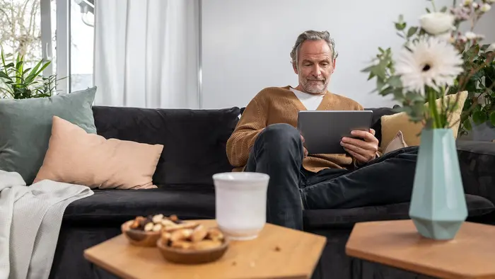 Mann sitzt auf Sofa und schaut auf Tablet