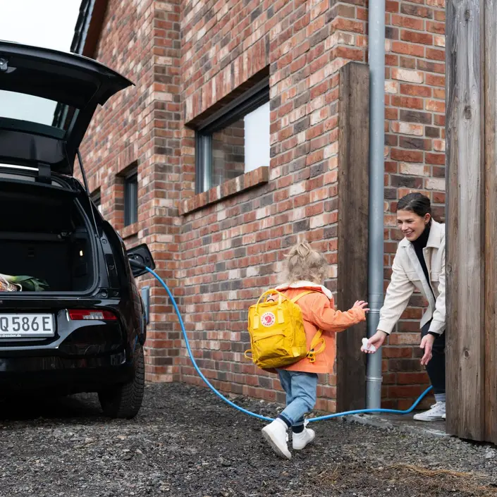 Eine Kind und eine Frau neben einem ladenden E-Auto.