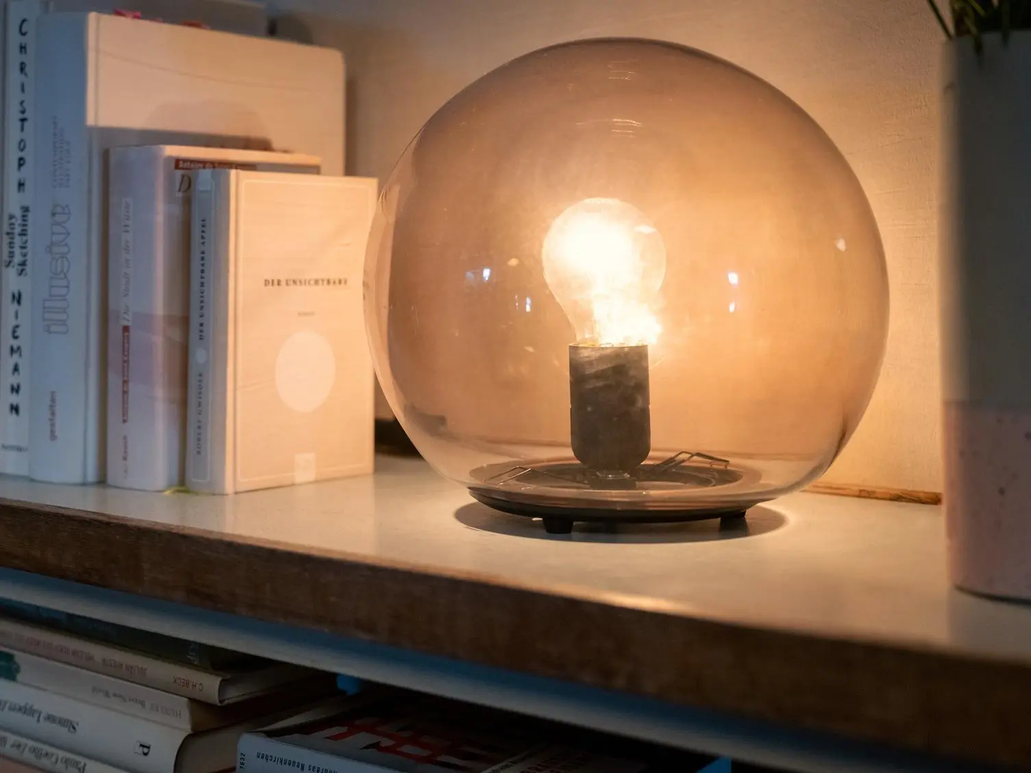 Beleuchtete Tischlampe auf einem Regal neben Büchern.