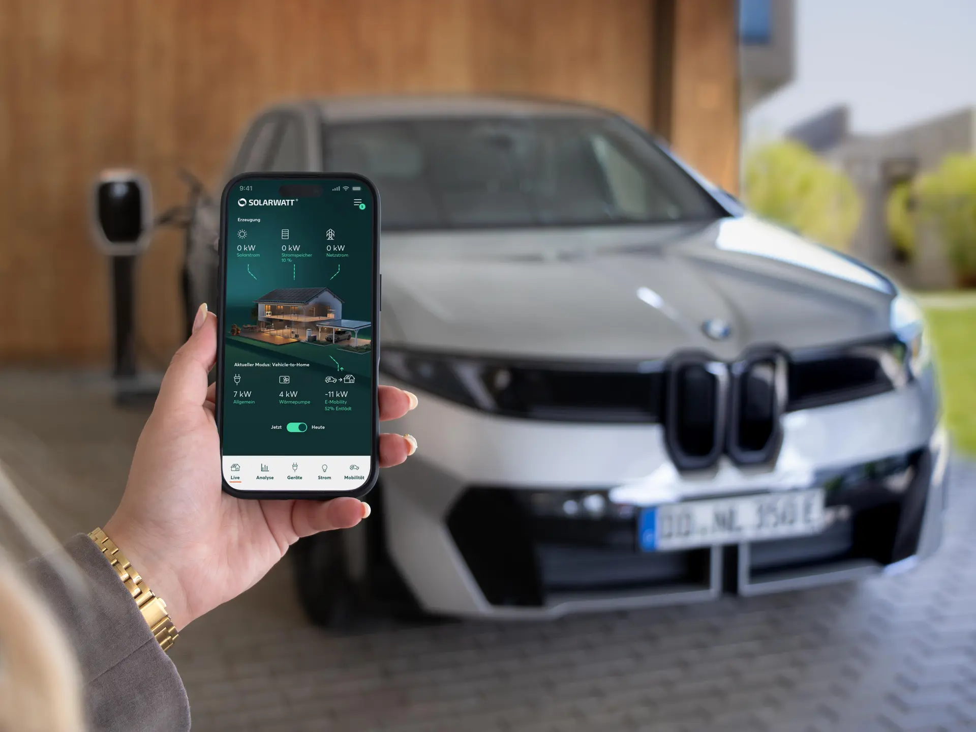 Home-Bildschirm der SOLARWATT Home app vor einem BMW-Fahrzeug